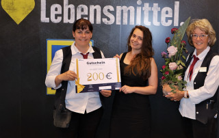 Übergabe des Blumenstraußes und des Einkaufsschecks an Frau Dorle Groth. Inhaberin des Edeka Marktes in Neustrelitz.